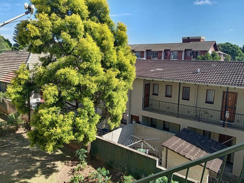 Elevated view overlooking the apartment complex grounds, featuring tiled roofing, security fencing, and established trees within the residential courtyard area.