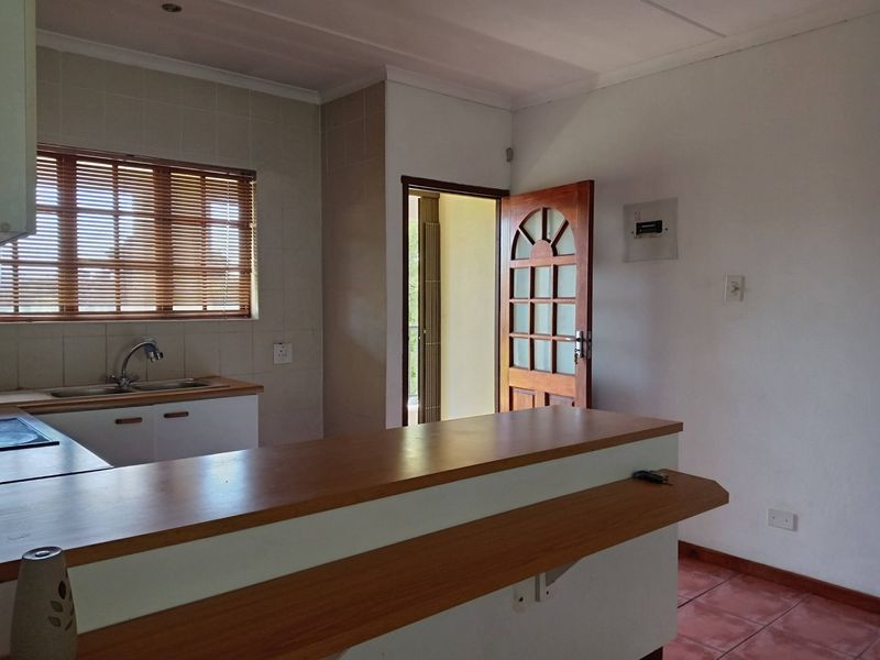 A functional kitchen area featuring a wooden breakfast bar, tiled splashback, double sink, and direct access to an adjacent room.