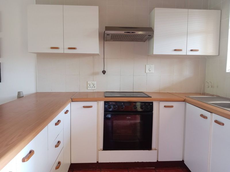 A functional kitchen featuring white cabinetry, laminate countertops, a built-in oven with electric hob, and a tiled backsplash.