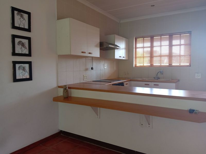 A functional kitchen featuring built-in cabinetry, a breakfast bar, tiled backsplash, and a stainless steel sink with a window view.