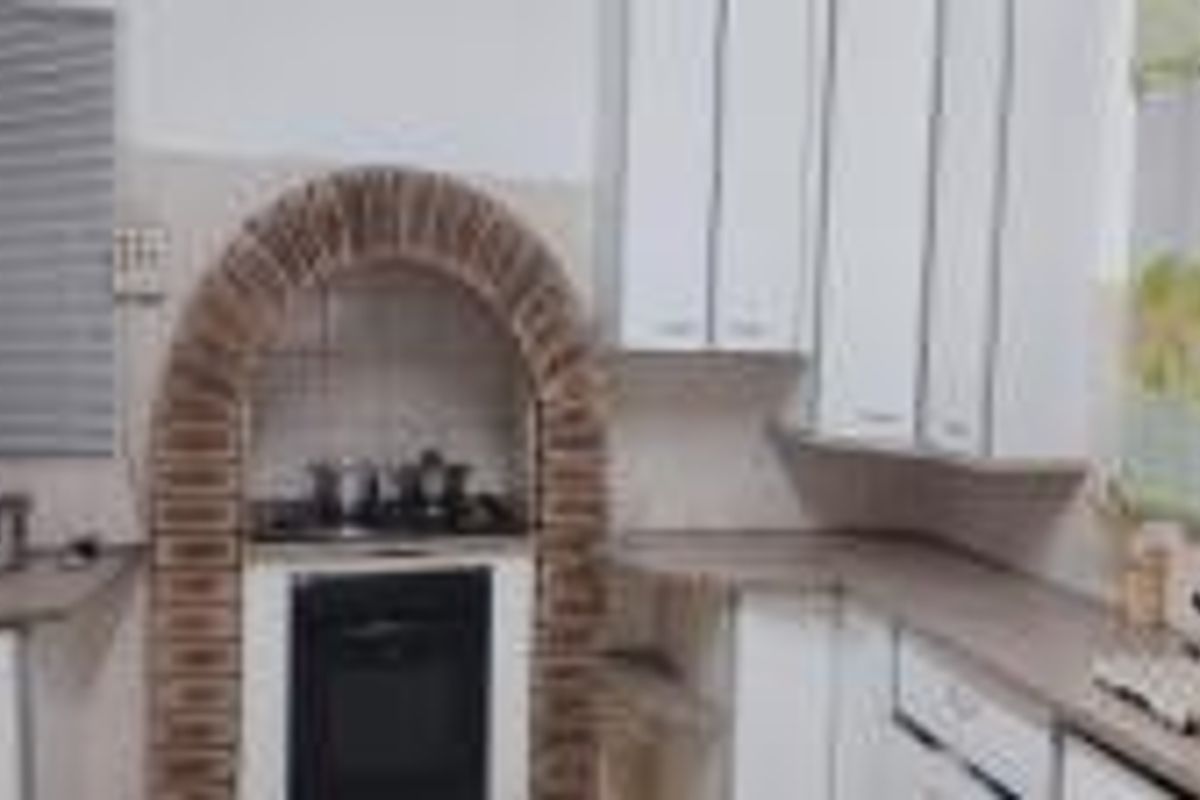 A functional kitchen featuring white cabinetry, laminate countertops, and a distinctive brick arch surrounding the built-in oven and hob area.
