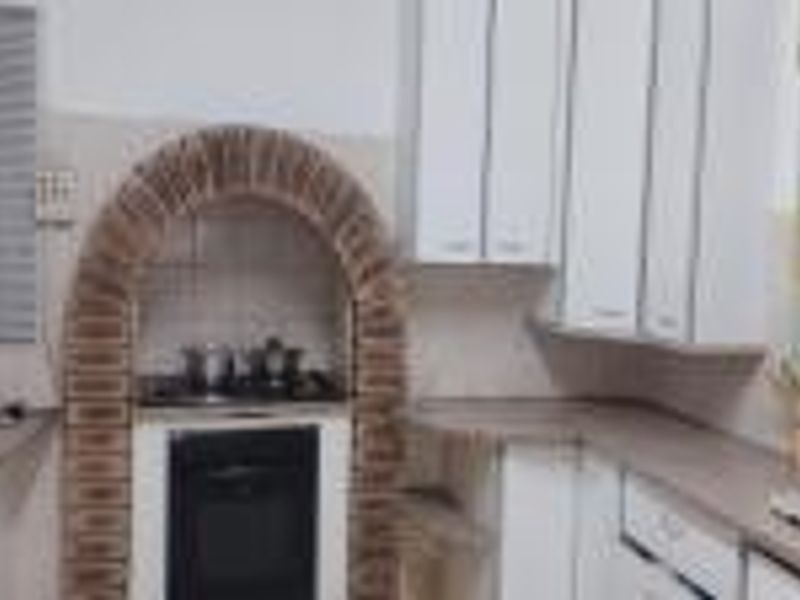 A functional kitchen featuring white cabinetry, laminate countertops, and a distinctive brick arch surrounding the built-in oven and hob area.