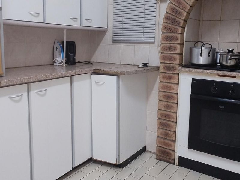 A dated kitchen featuring white cabinetry, laminate countertops, a tiled backsplash, and a distinctive brick archway surrounding the built-in oven and hob.