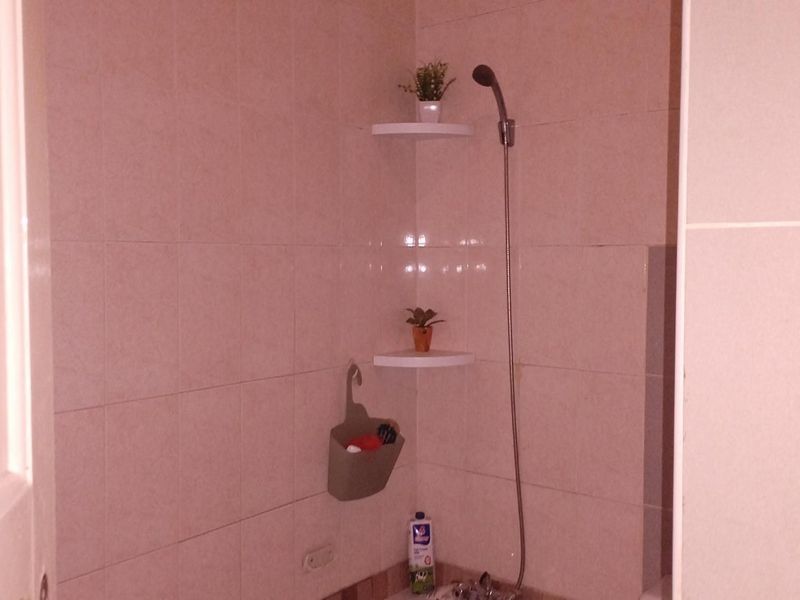 A functional bathroom shower area featuring wall-mounted corner shelving and a standard shower fixture with tiled wall finishes.