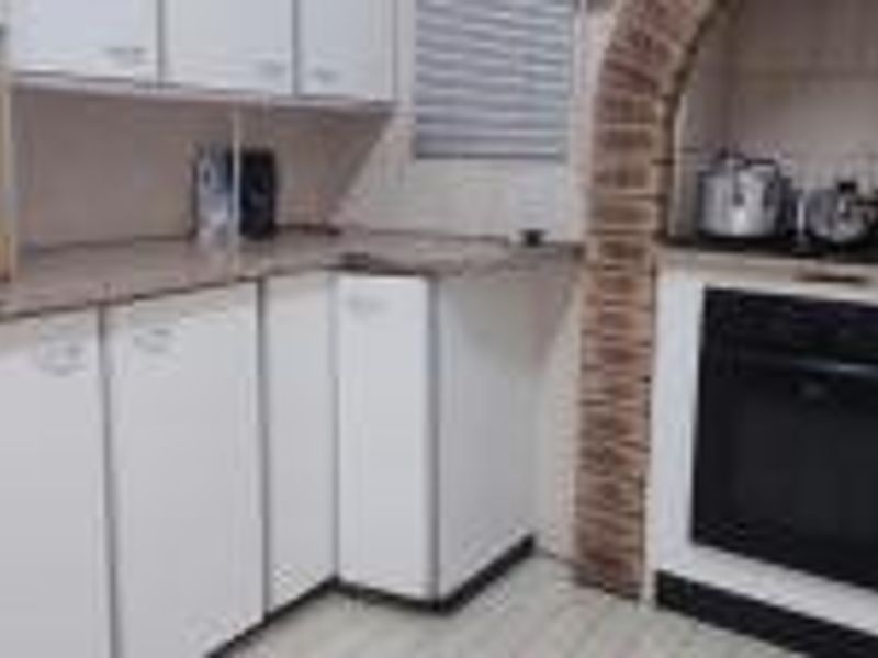 A functional kitchen featuring white cabinetry, laminate countertops, and a distinctive brick arch surrounding the built-in oven and hob area.