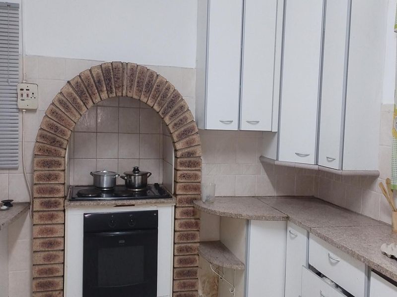 Kitchen featuring a distinctive brick arch over the built-in oven and hob, complemented by white cabinetry and tiled backsplash.