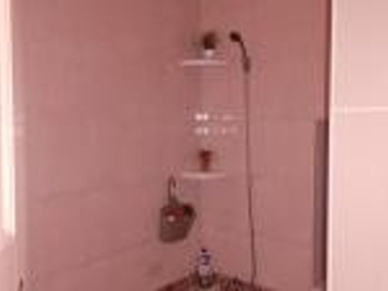 A simple bathroom shower area featuring tiled walls, a handheld shower head, and built-in corner shelving.