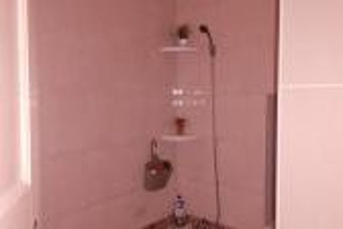 A simple bathroom shower area featuring tiled walls, a handheld shower head, and built-in corner shelving.