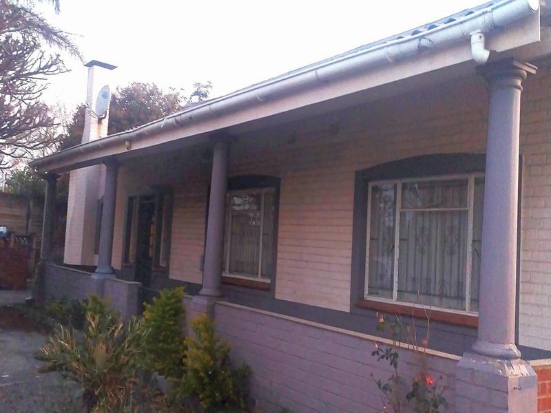 Front elevation of a single-story house featuring a covered veranda with decorative columns, brick facade, and security bars on the windows.