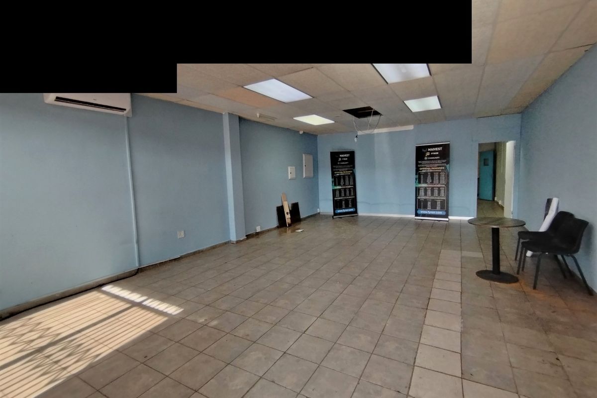 An empty, open-plan commercial or living space featuring ceramic tile flooring, a drop ceiling with recessed lighting, and a wall-mounted air conditioning unit.