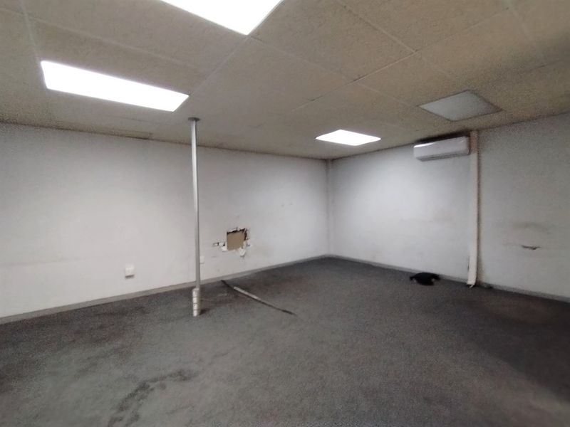An empty utility space featuring a suspended ceiling, recessed lighting, a wall-mounted air conditioning unit, and a central support column.