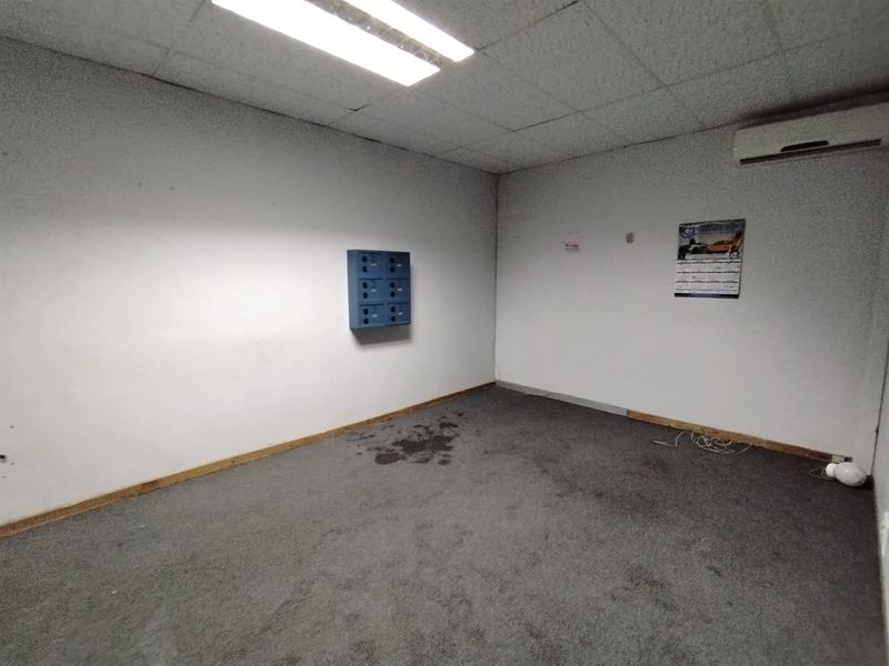 An empty utility space featuring a drop ceiling, carpeted flooring, wall-mounted mailboxes, and a split-system air conditioner unit.