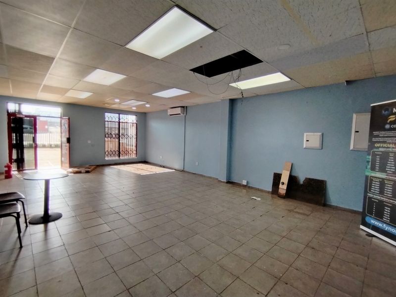 An open-plan utility or commercial space featuring tiled flooring, a drop ceiling with recessed lighting, and a wall-mounted air conditioning unit.