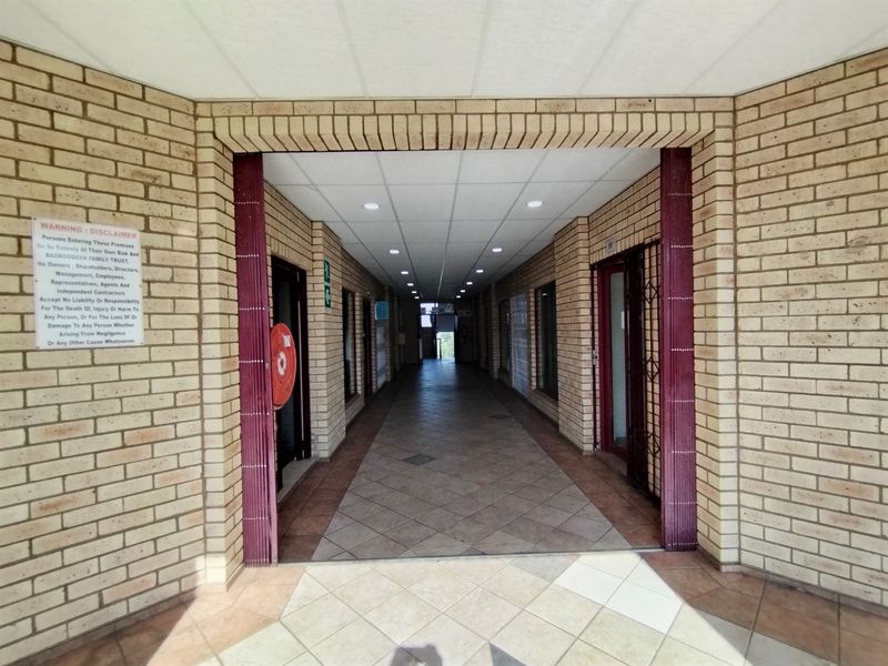 A long, tiled hallway featuring exposed brick walls and recessed ceiling lighting, providing access to multiple entry points.