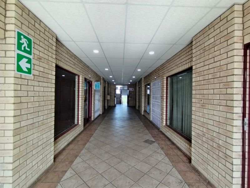 A long, tiled hallway featuring exposed brick walls, a suspended ceiling with recessed lighting, and security gates, providing access to multiple units.