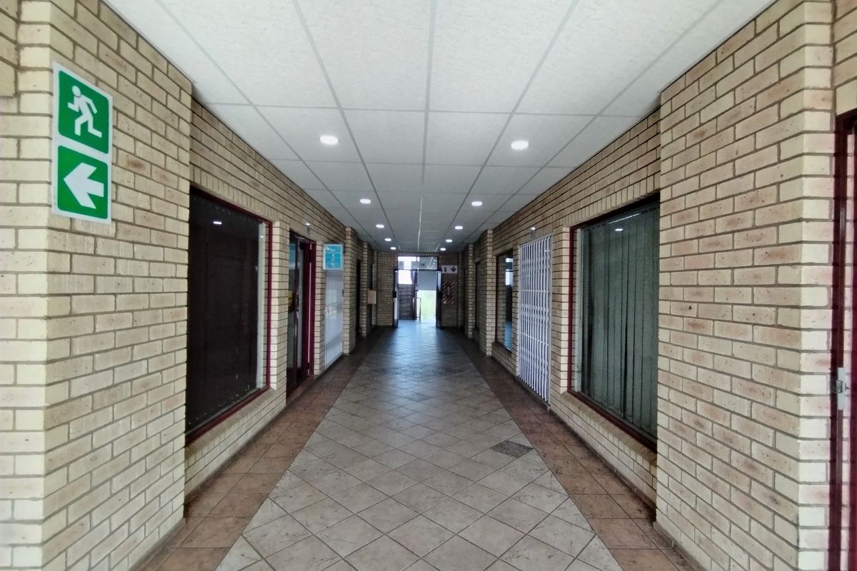A long, tiled hallway featuring exposed brick walls, a suspended ceiling with recessed lighting, and security gates, providing access to multiple units.