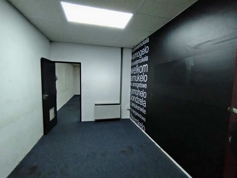 An empty office space featuring a suspended ceiling, recessed lighting, HVAC unit, and dark carpet flooring with a decorative feature wall.