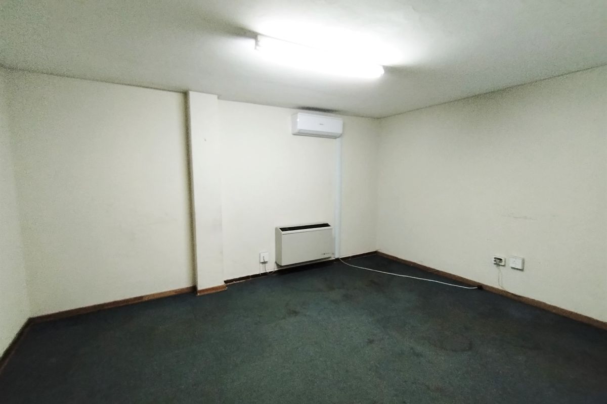 An empty bedroom featuring a wall-mounted air conditioner, built-in heater, and carpeted flooring, offering a blank canvas for renovation or restyling.