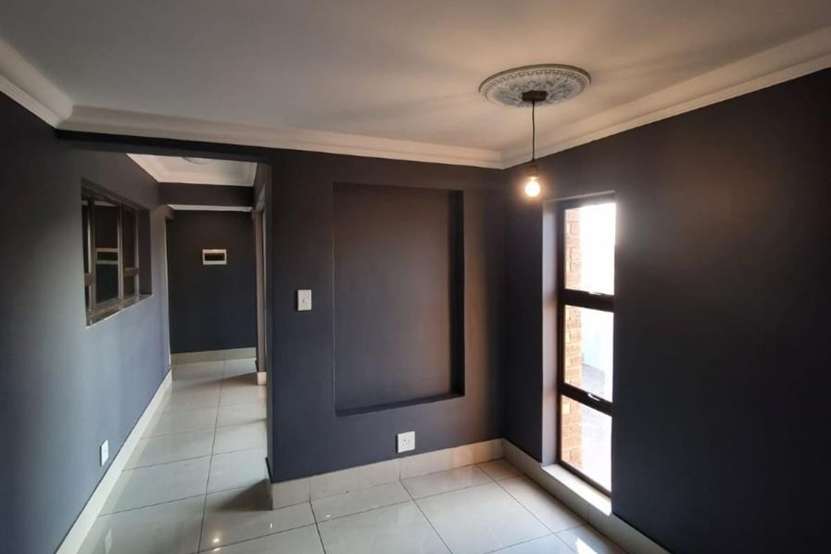 A bright, empty living area featuring modern tiled flooring, a decorative ceiling rose, and a built-in wall niche, leading into a hallway.