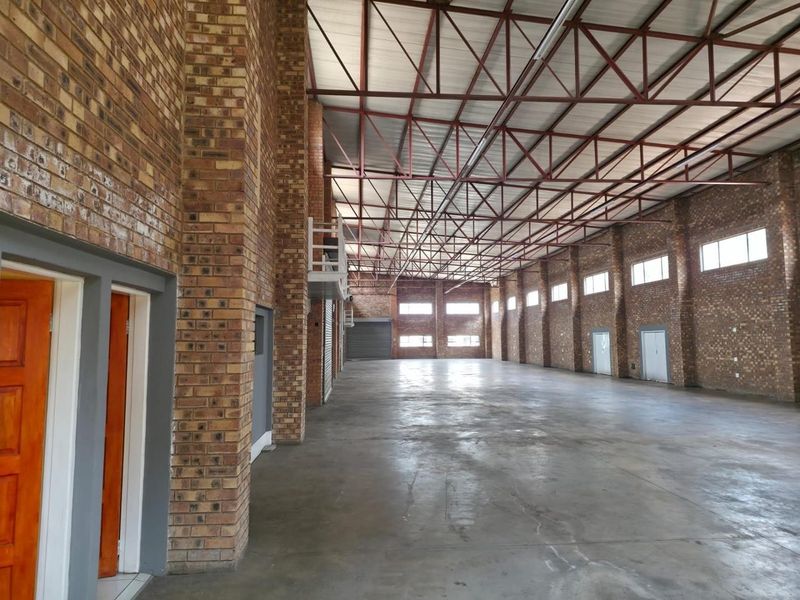 Spacious industrial warehouse unit featuring exposed brick walls, high steel roof trusses, concrete flooring, and multiple access points for efficient operations.