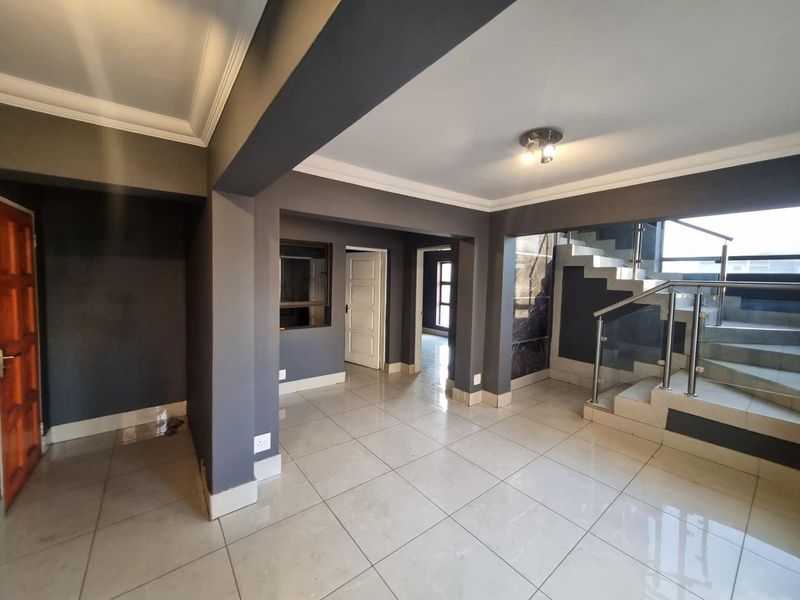 Spacious open-plan interior area featuring modern tiled flooring, a contemporary staircase with stainless steel railings, and neutral grey wall finishes.