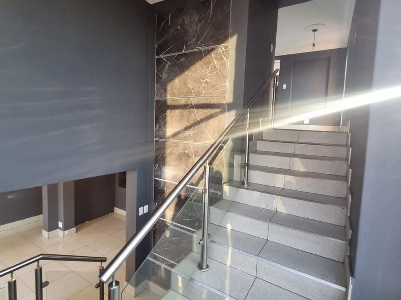 Modern interior hallway featuring a tiled staircase with a glass balustrade, stainless steel handrail, and decorative marble-effect wall cladding.