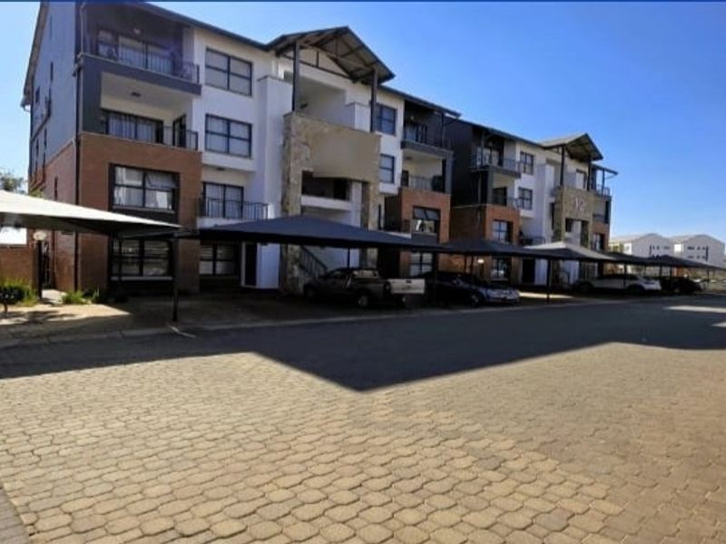 Exterior view of a multi-story apartment complex featuring paved parking areas with shade cloth carports and private balconies.
