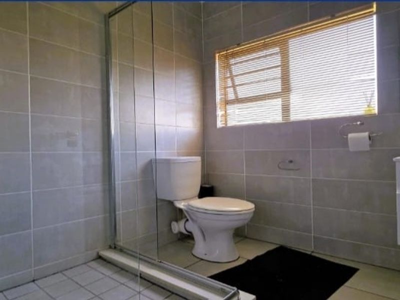 A clean, modern bathroom featuring a glass-enclosed shower, a wall-mounted vanity, and neutral wall tiling.