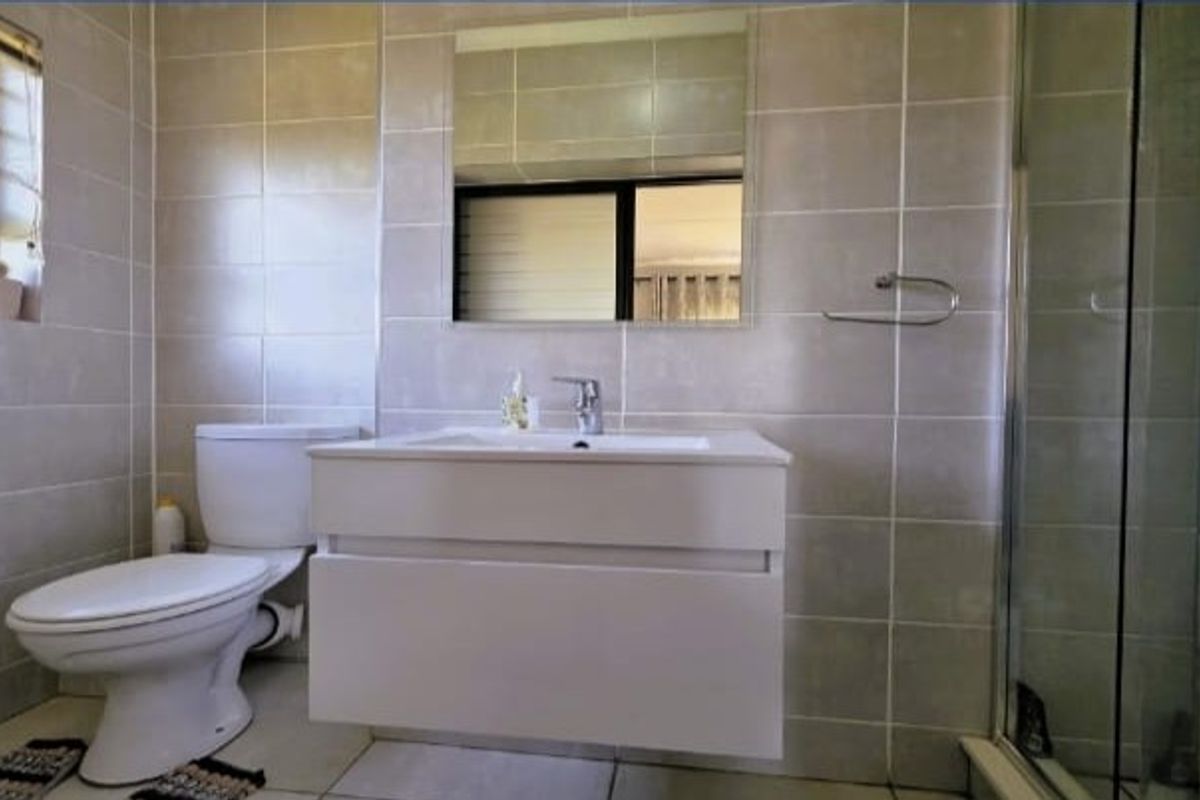 A modern bathroom featuring a wall-mounted vanity, a glass shower enclosure, and neutral wall tiling.