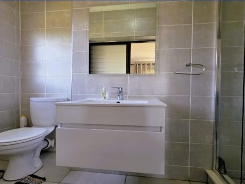 A modern bathroom featuring a wall-mounted vanity, a glass shower enclosure, and neutral wall tiling.