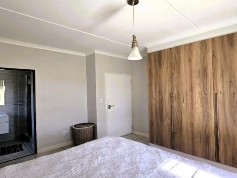 A well-maintained bedroom featuring modern wood-finish built-in cupboards, neutral wall tones, and direct access to an en-suite bathroom.