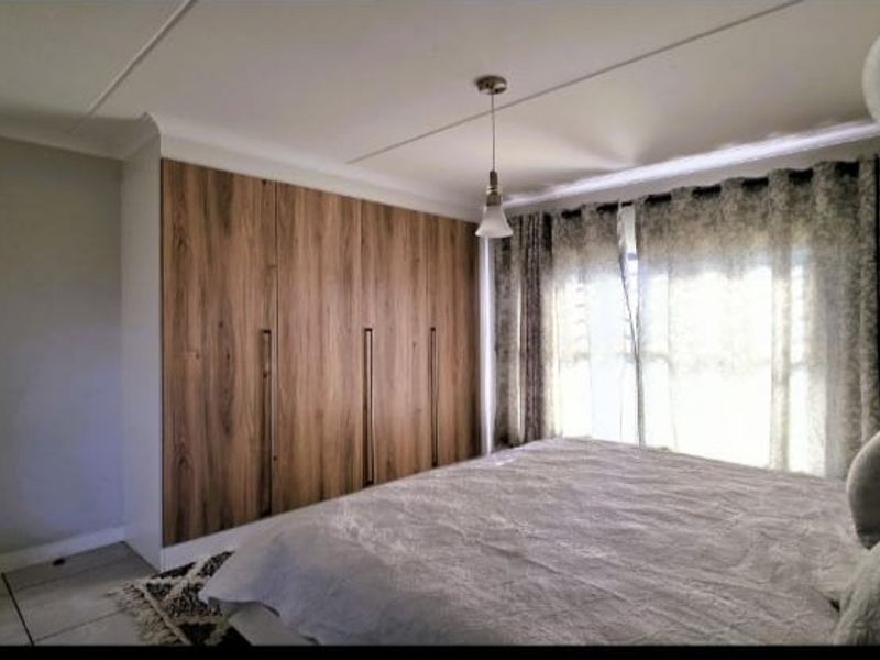 A well-maintained bedroom featuring modern wood-finish built-in cupboards, tiled flooring, and a pendant light fixture.