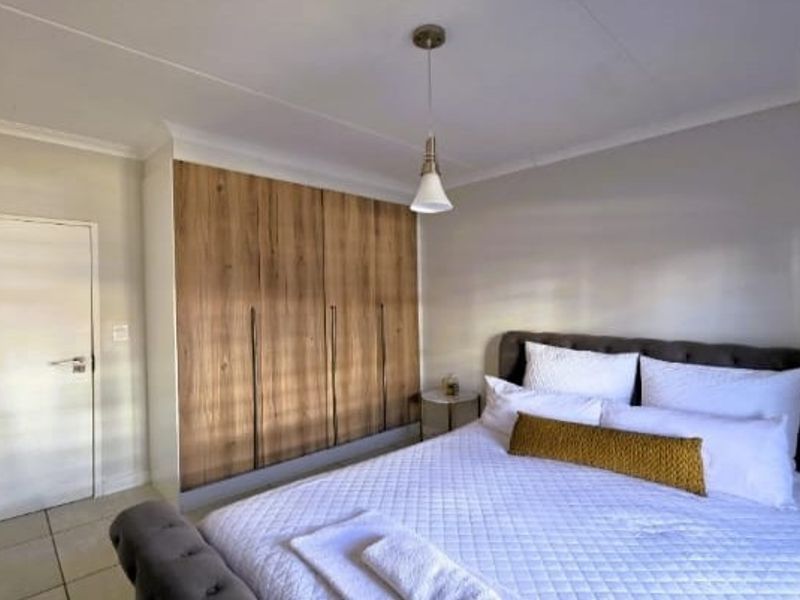 A well-maintained bedroom featuring modern wood-finish built-in cupboards, neutral tiled flooring, and a clean, contemporary aesthetic.