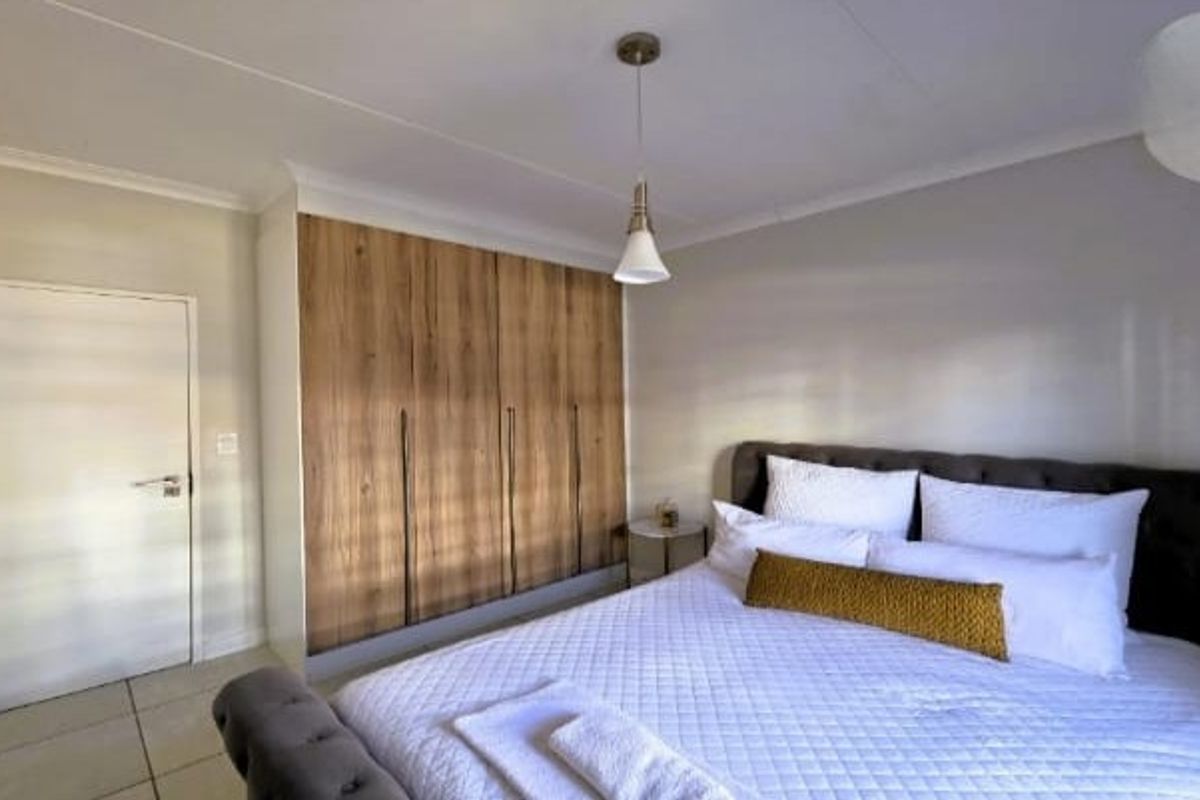 A well-maintained bedroom featuring modern wood-finish built-in cupboards, neutral tiled flooring, and a clean, contemporary aesthetic.