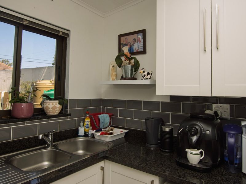 A functional kitchen area featuring dark granite countertops, a double bowl stainless steel sink, and a modern grey subway tile backsplash.