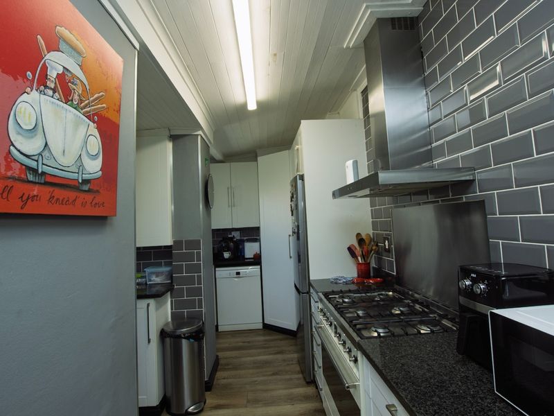 A functional kitchen featuring granite countertops, a gas hob with stainless steel extractor, subway tile backsplash, and modern timber-look flooring.
