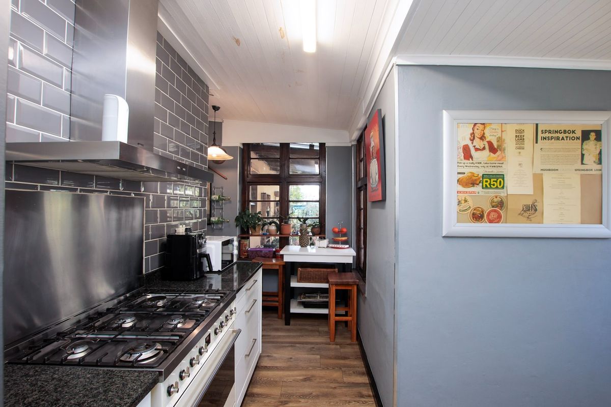 A functional kitchen featuring a gas hob, stainless steel extractor, granite countertops, and subway tile backsplash with timber-paneled ceilings and wood-look flooring.