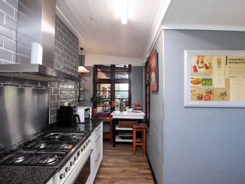 A functional kitchen featuring a gas hob, stainless steel extractor, granite countertops, and subway tile backsplash with timber-paneled ceilings and wood-look flooring.