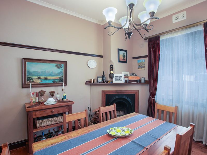 A charming dining room featuring a traditional fireplace with a timber mantelpiece, polished timber flooring, and classic picture rails.
