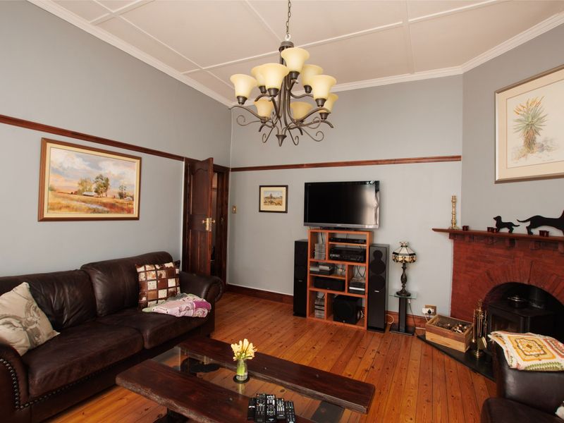 A cozy living room featuring original exposed timber flooring, a classic brick fireplace, and decorative coffered ceilings with a traditional chandelier.