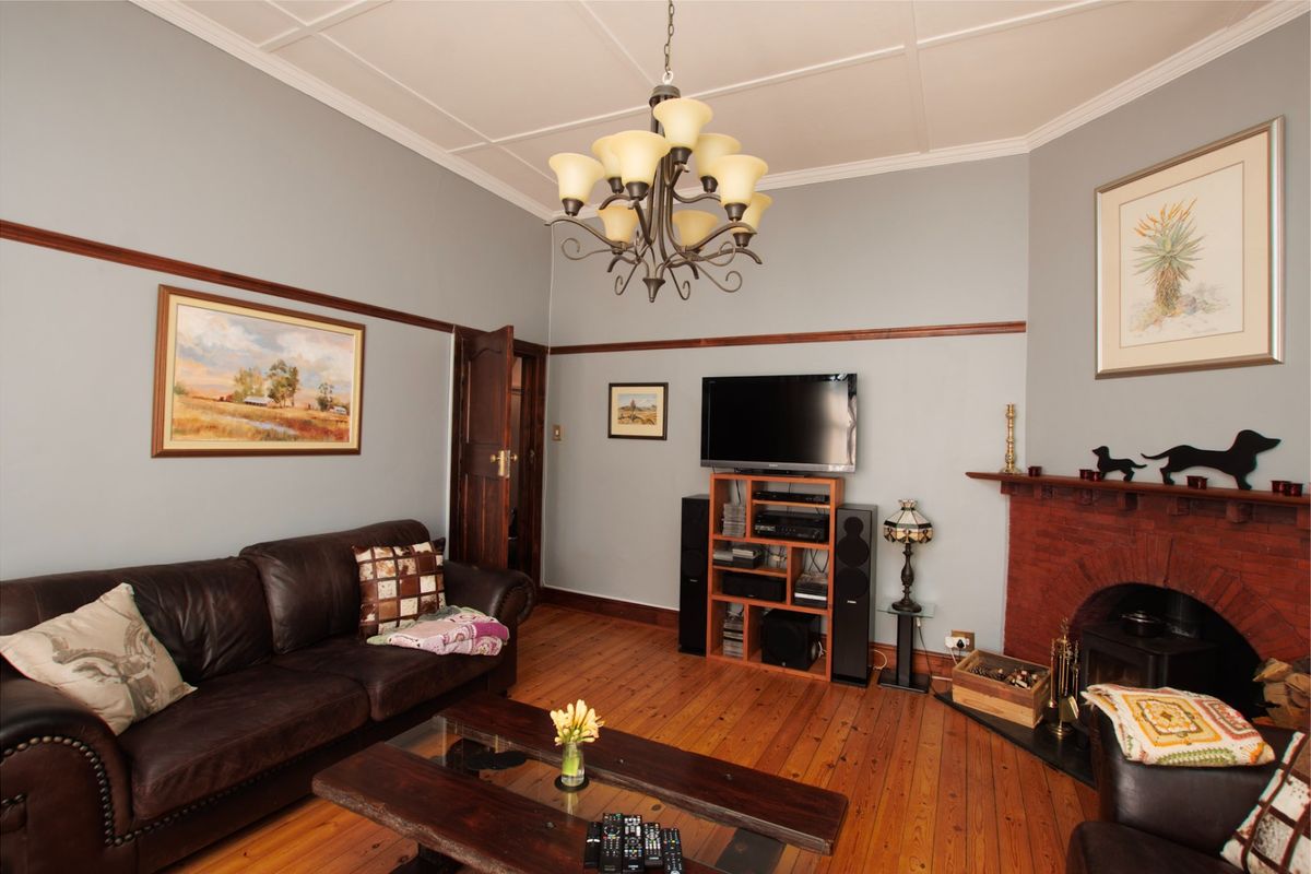 A cozy living room featuring original exposed timber flooring, a classic brick fireplace, and decorative coffered ceilings with a traditional chandelier.