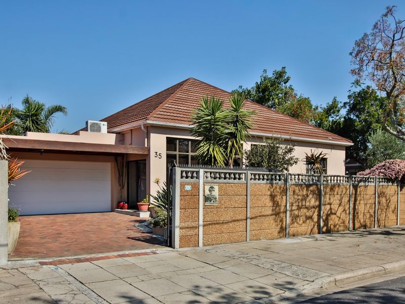 Front elevation of a single-story house featuring a tiled roof, paved driveway, attached garage, and a secure precast concrete boundary wall.