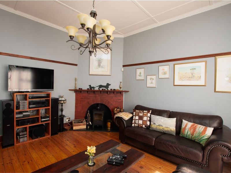 A cozy living room featuring original timber flooring, a classic brick fireplace with a wood-burning stove, and elegant coffered ceilings.