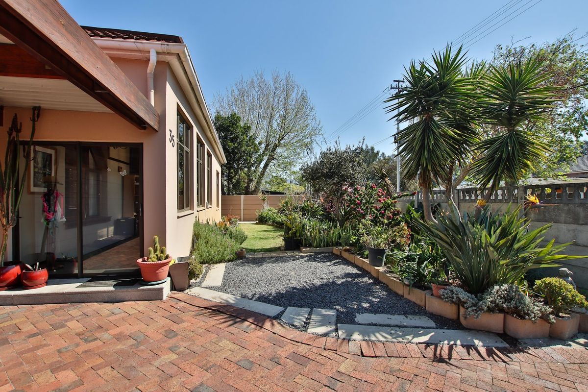 Rear exterior view featuring a brick paved patio, gravel garden section, and established landscaping with a concrete boundary wall.