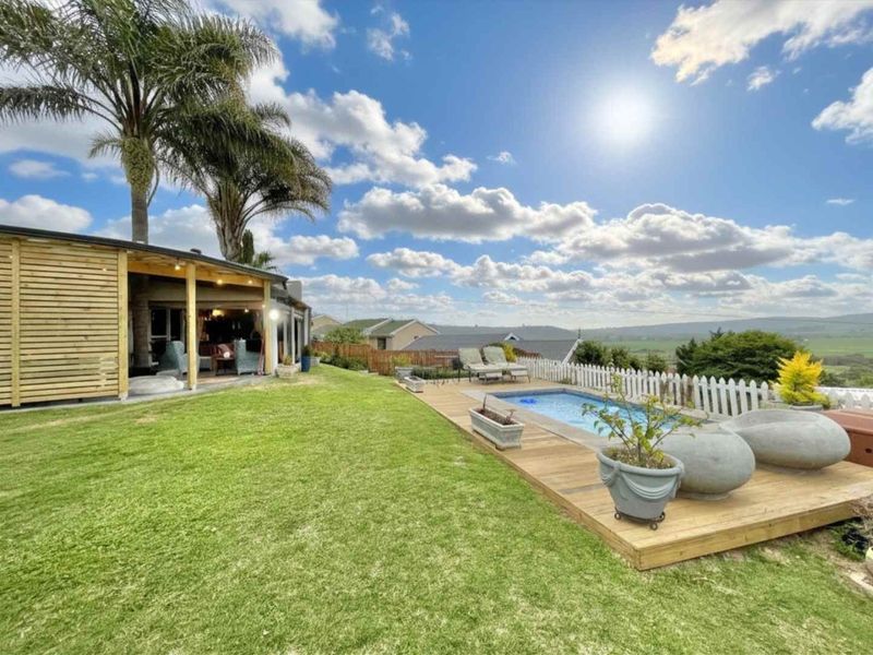 Outdoor entertainment area featuring a swimming pool with timber decking, a covered patio, and a well-maintained lawn with scenic views.