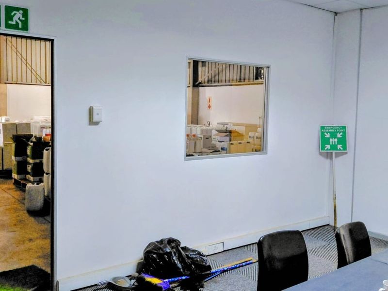 An office space featuring an internal viewing window looking into the warehouse area, equipped with standard safety signage and electrical infrastructure.
