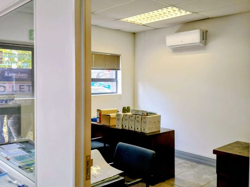 A functional office space featuring a suspended ceiling, recessed lighting, and a wall-mounted air conditioning unit, providing a practical work environment.