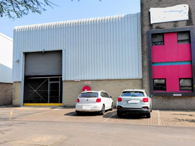 Front elevation of an industrial warehouse unit featuring a large roller shutter door, corrugated metal cladding, and dedicated paved parking space.