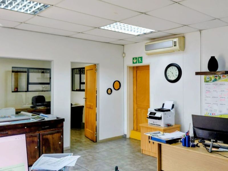 Functional office space featuring a suspended ceiling, recessed lighting, wall-mounted air conditioning, and a glass partition for visibility into adjacent areas.