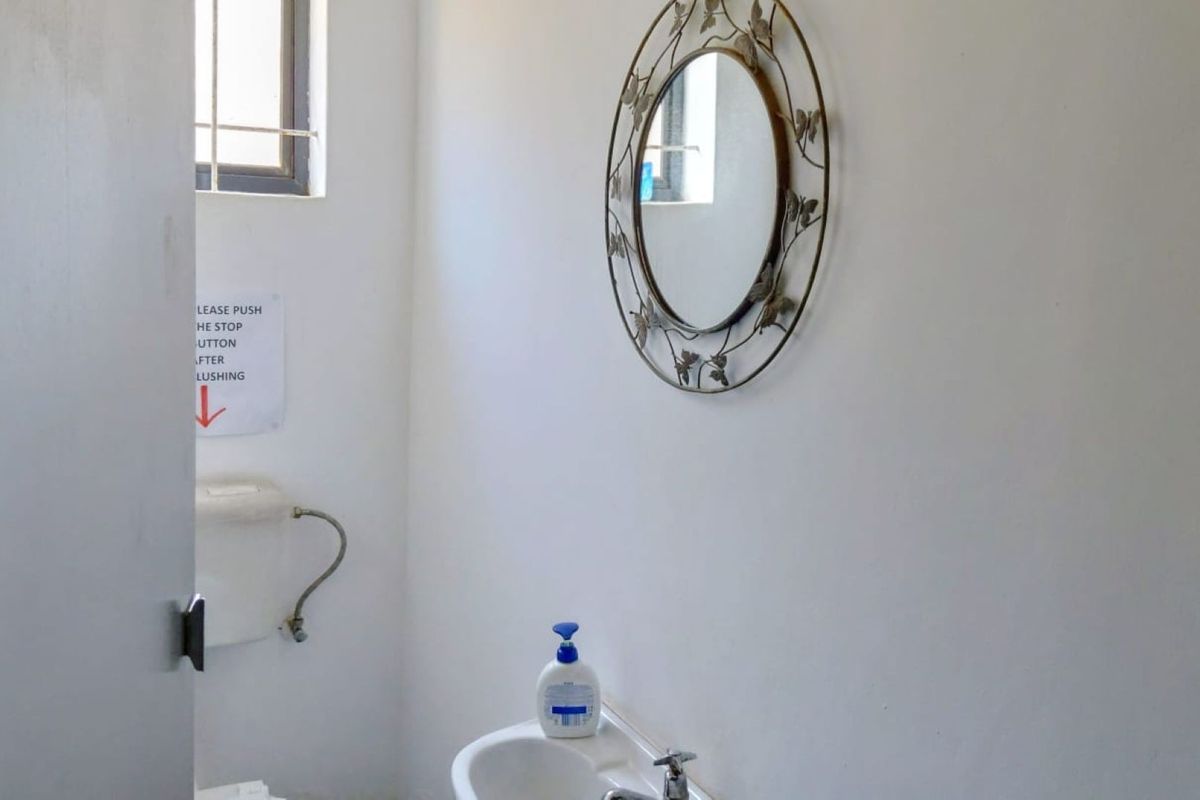 A functional bathroom featuring a standard toilet, wall-mounted washbasin, and a small window with security bars.